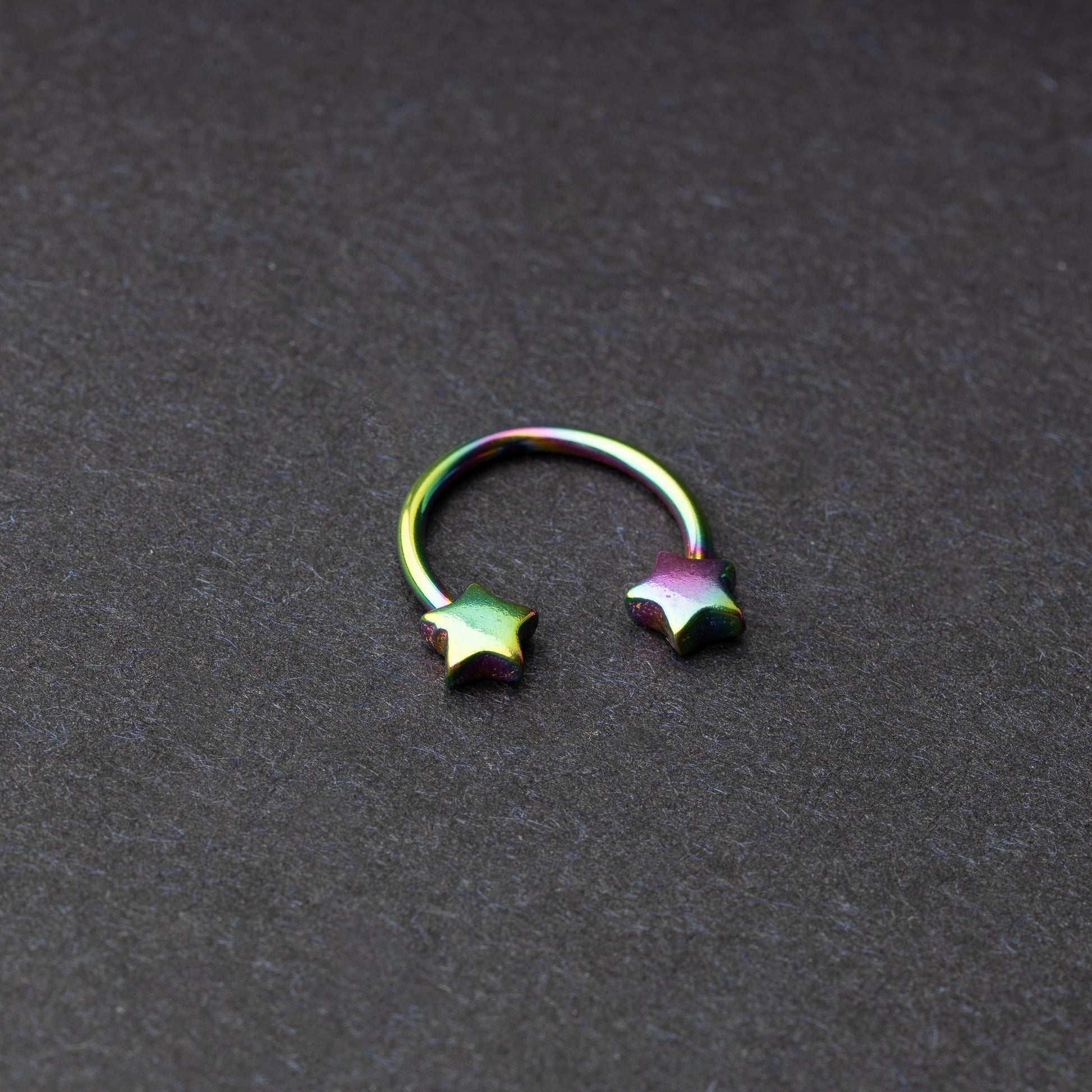 Stainless steel horseshoe hoop with star-shaped ends in rainbow, displayed on a dark background.