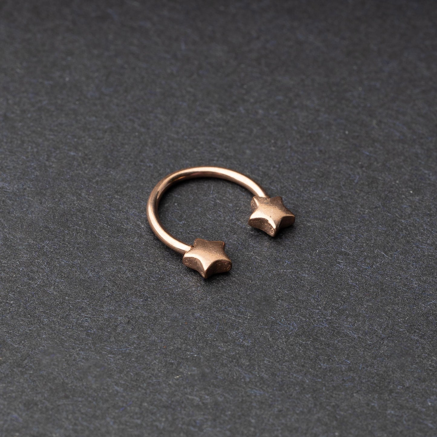 Stainless steel horseshoe hoop with star-shaped ends in rose gold, displayed on a dark background.