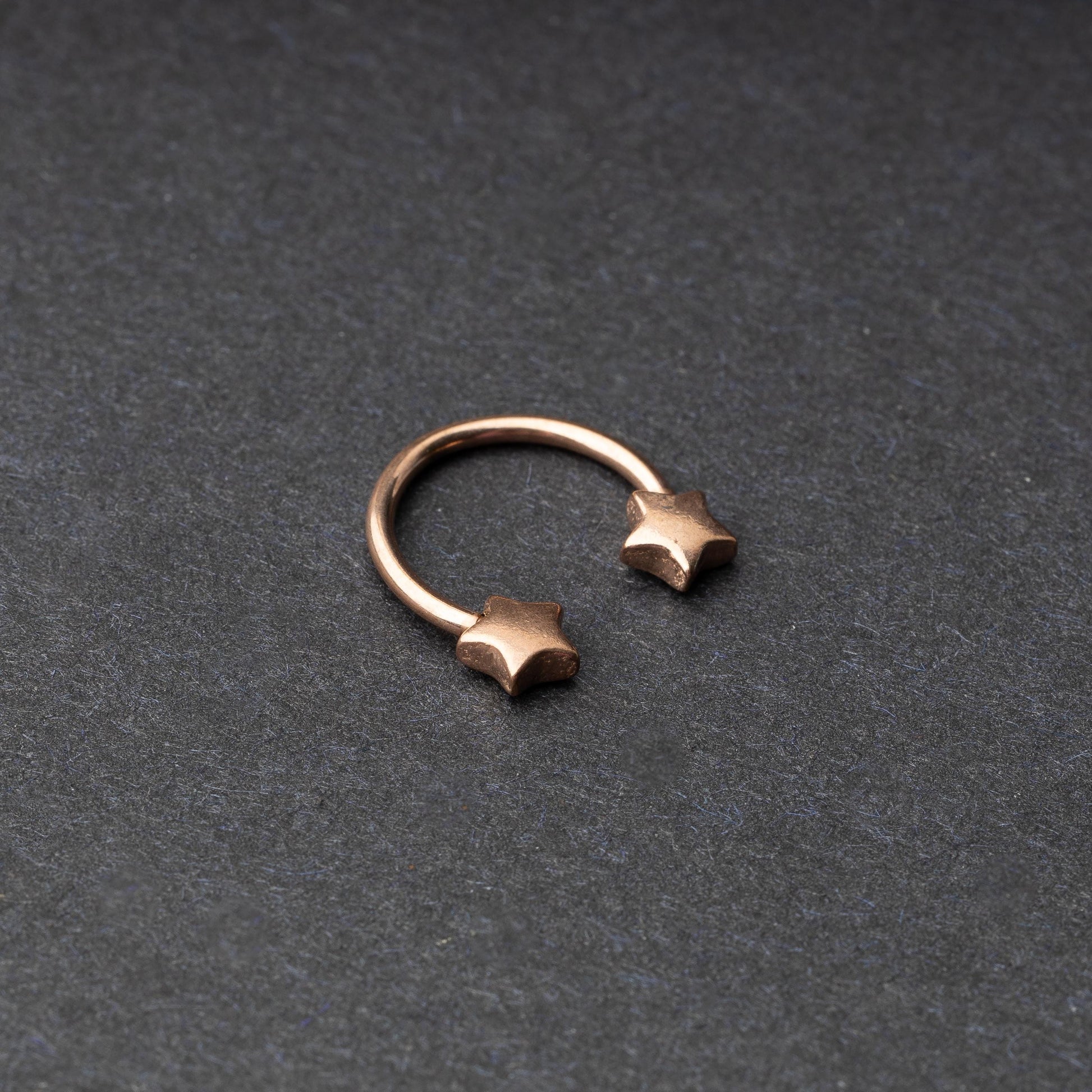Stainless steel horseshoe hoop with star-shaped ends in rose gold, displayed on a dark background.
