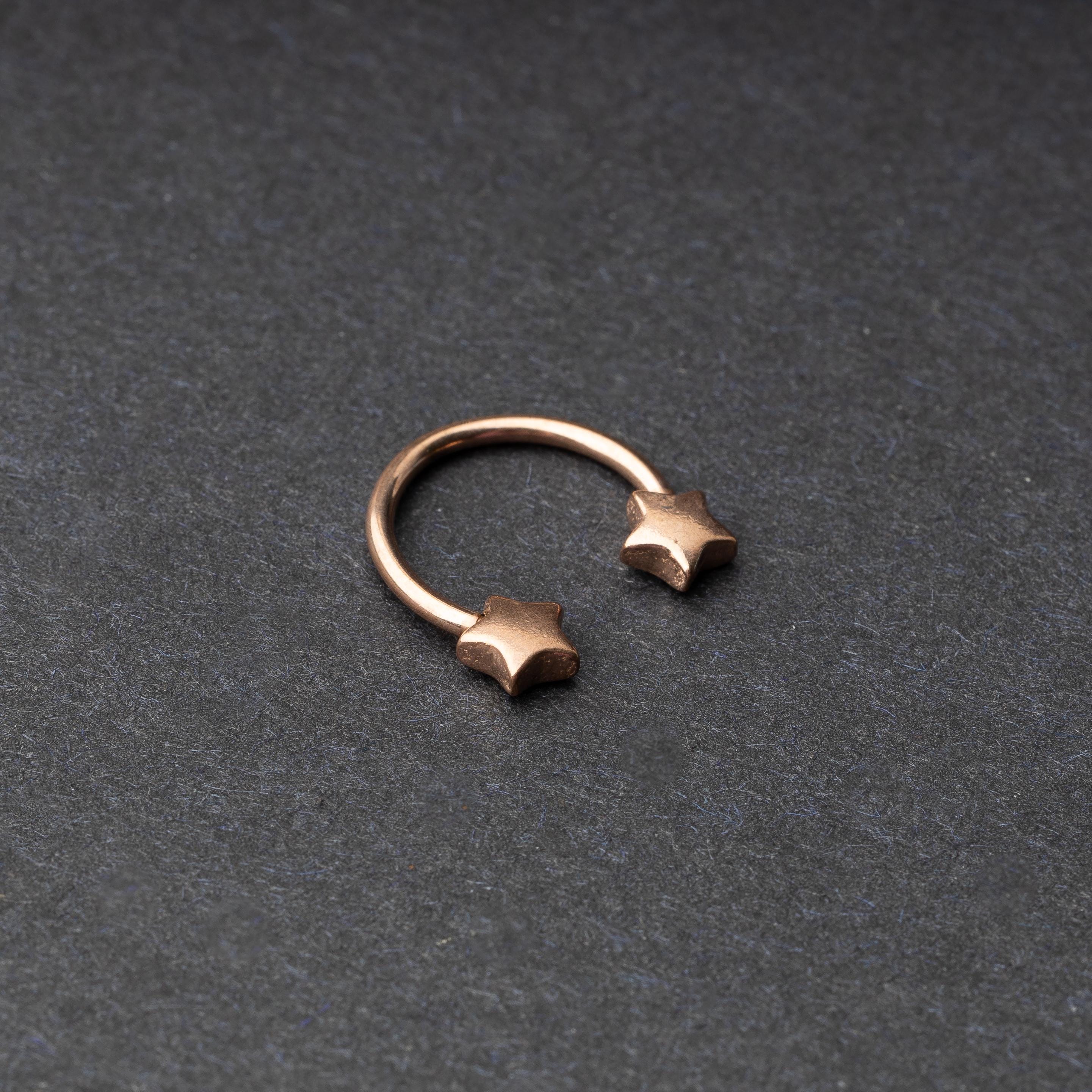 Stainless steel horseshoe hoop with star-shaped ends in rose gold, displayed on a dark background.