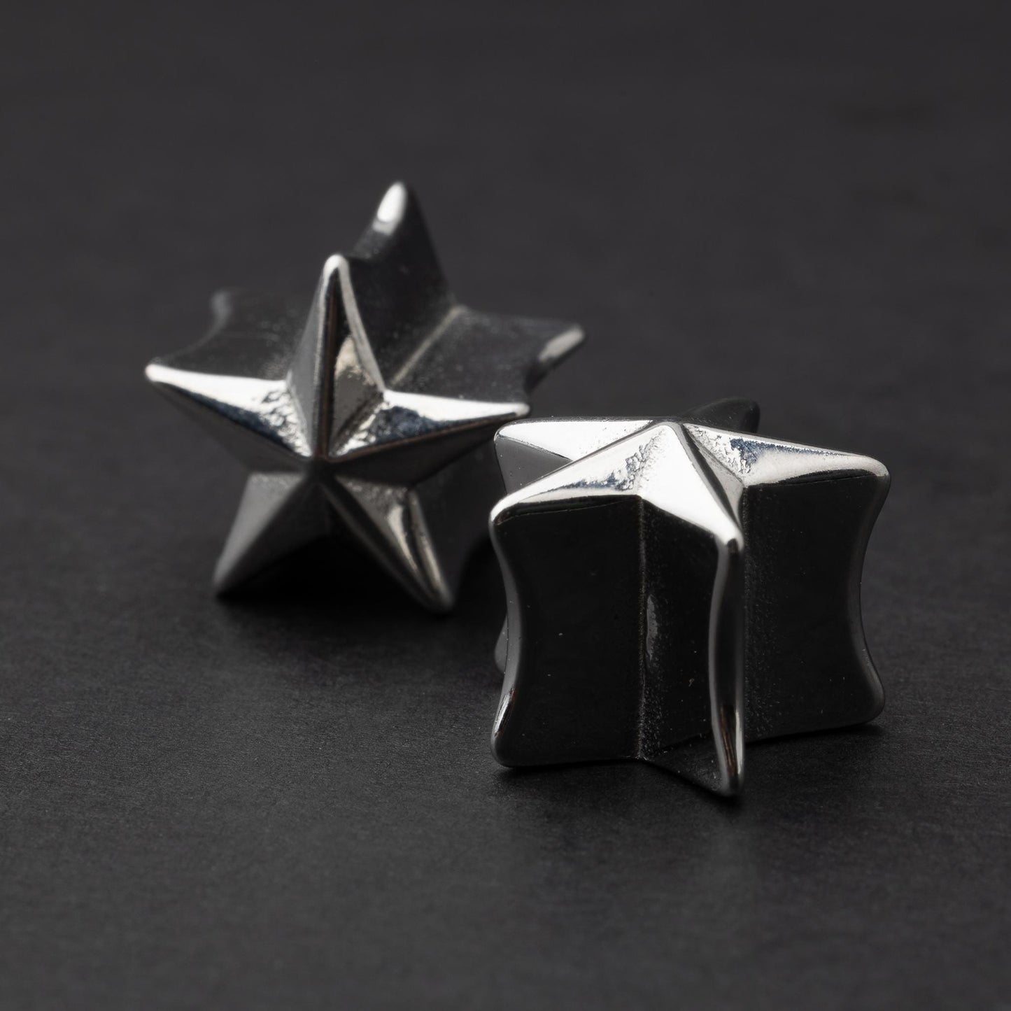 Stainless steel star-shaped plugs for stretched ears, displayed on a dark background.