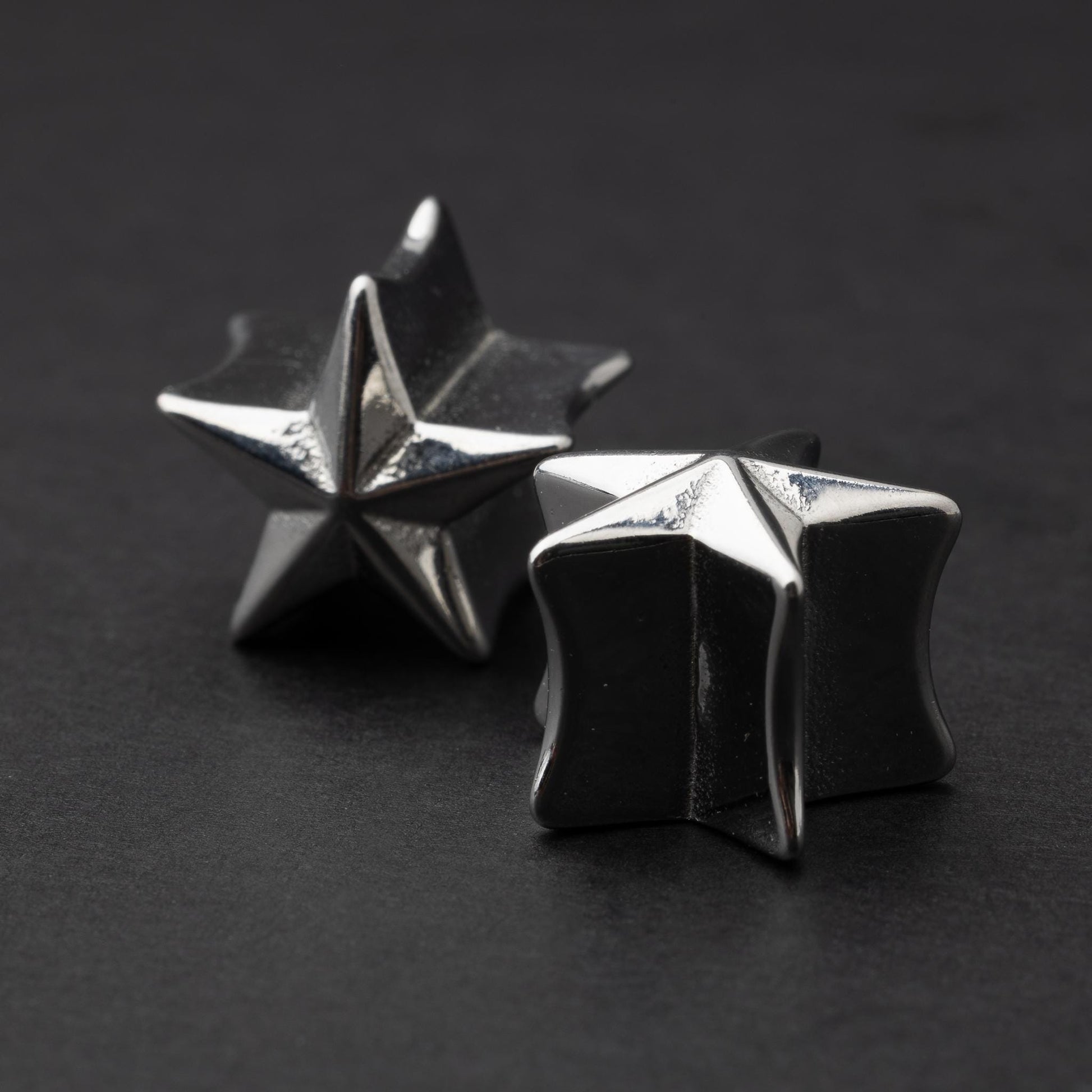 Stainless steel star-shaped plugs for stretched ears, displayed on a dark background.