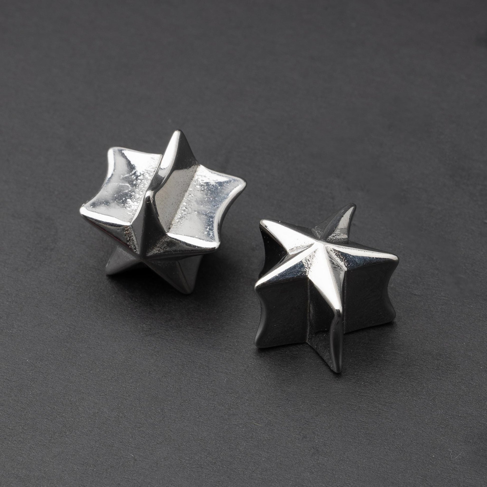 Stainless steel star-shaped plugs for stretched ears, displayed on a dark background.