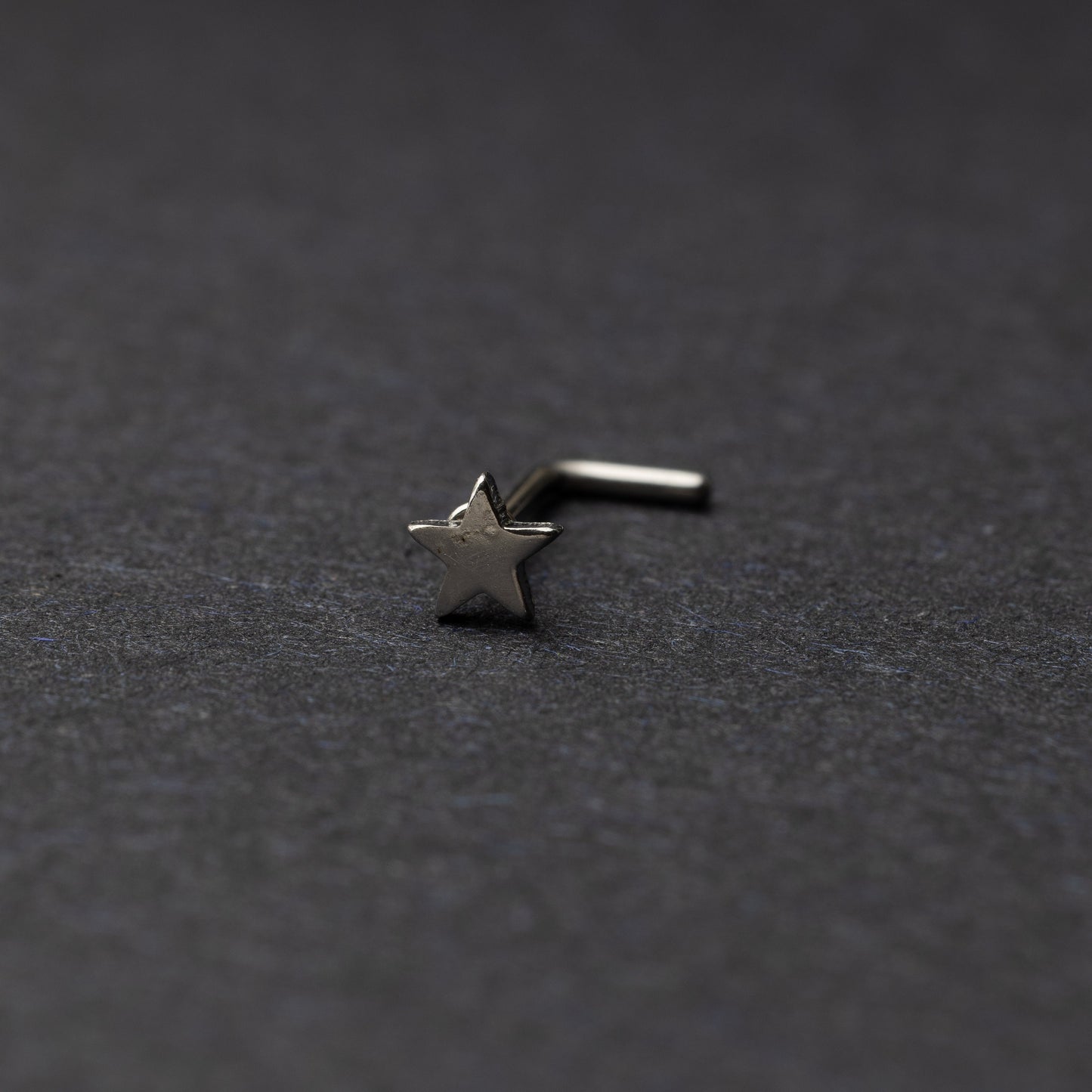 Sterling silver nose stud with a star-shaped design, displayed on a dark background.