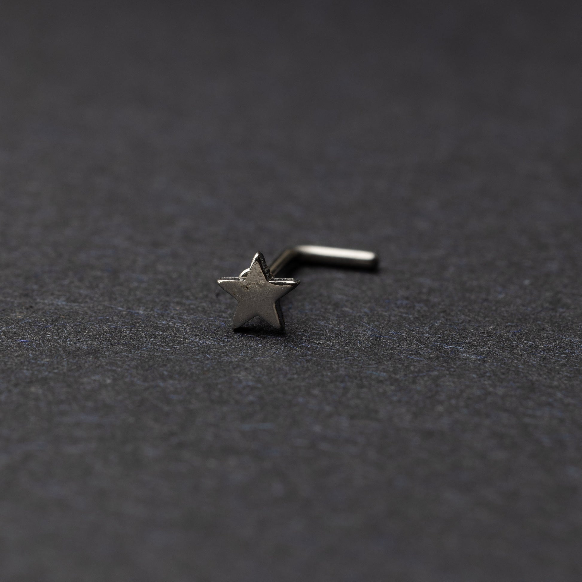 Sterling silver nose stud with a star-shaped design, displayed on a dark background.