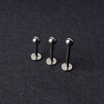 Three silver stainless steel labret studs with flat backs and polished ball ends, displayed on a dark textured background.