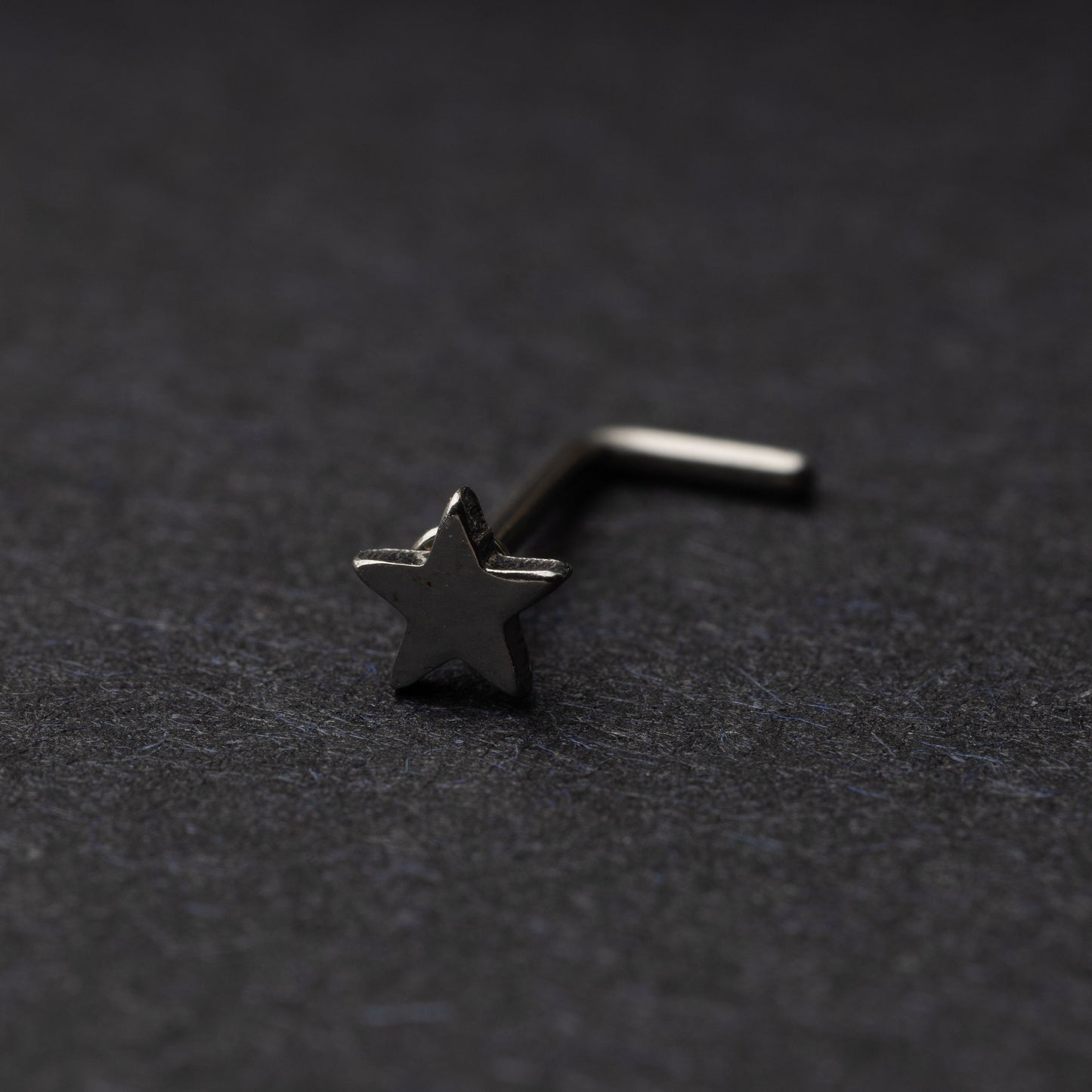 Sterling silver nose stud with a star-shaped design, displayed on a dark background.