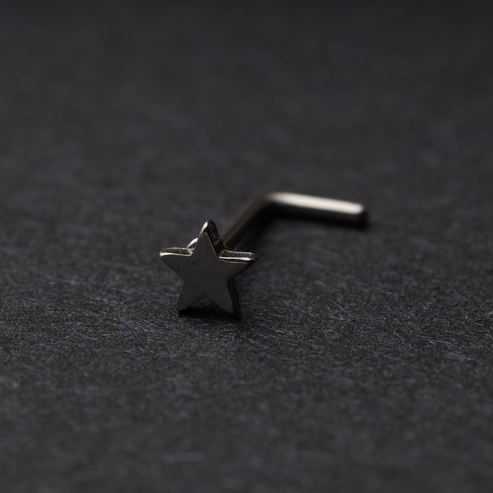 Sterling silver nose stud with a star-shaped design, displayed on a dark background.