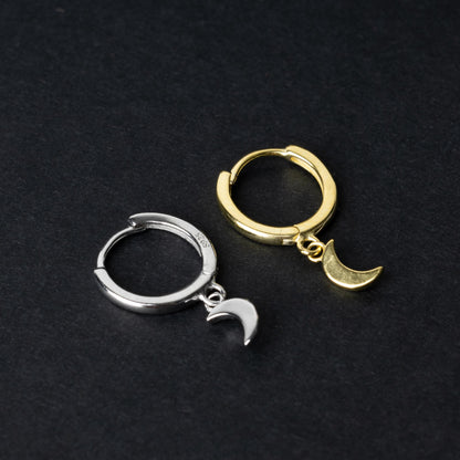 Two crescent moon huggie hoop earrings in gold and silver, each featuring a dangling crescent charm, displayed on a dark background.