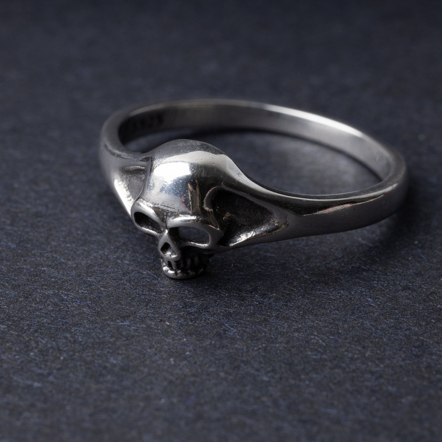 Sterling silver ring featuring a detailed skull design, displayed on a dark background.