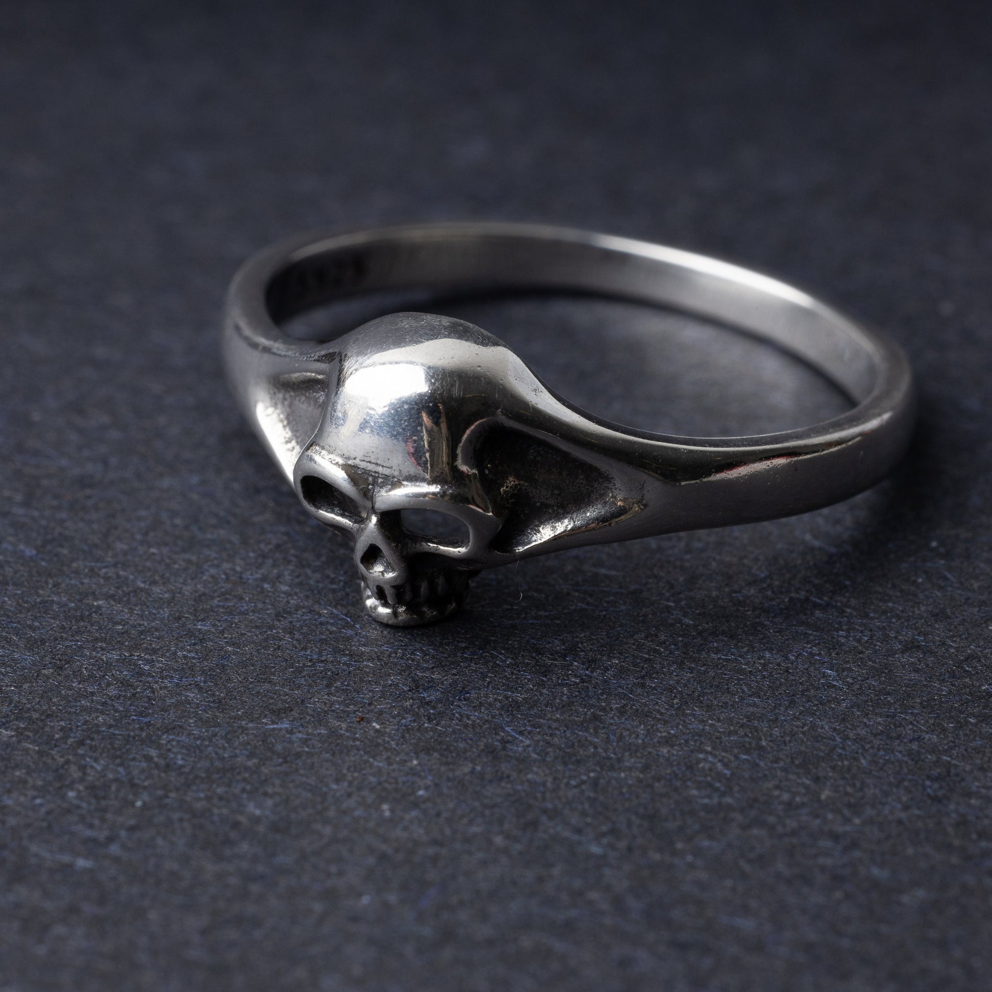 Sterling silver ring featuring a detailed skull design, displayed on a dark background.