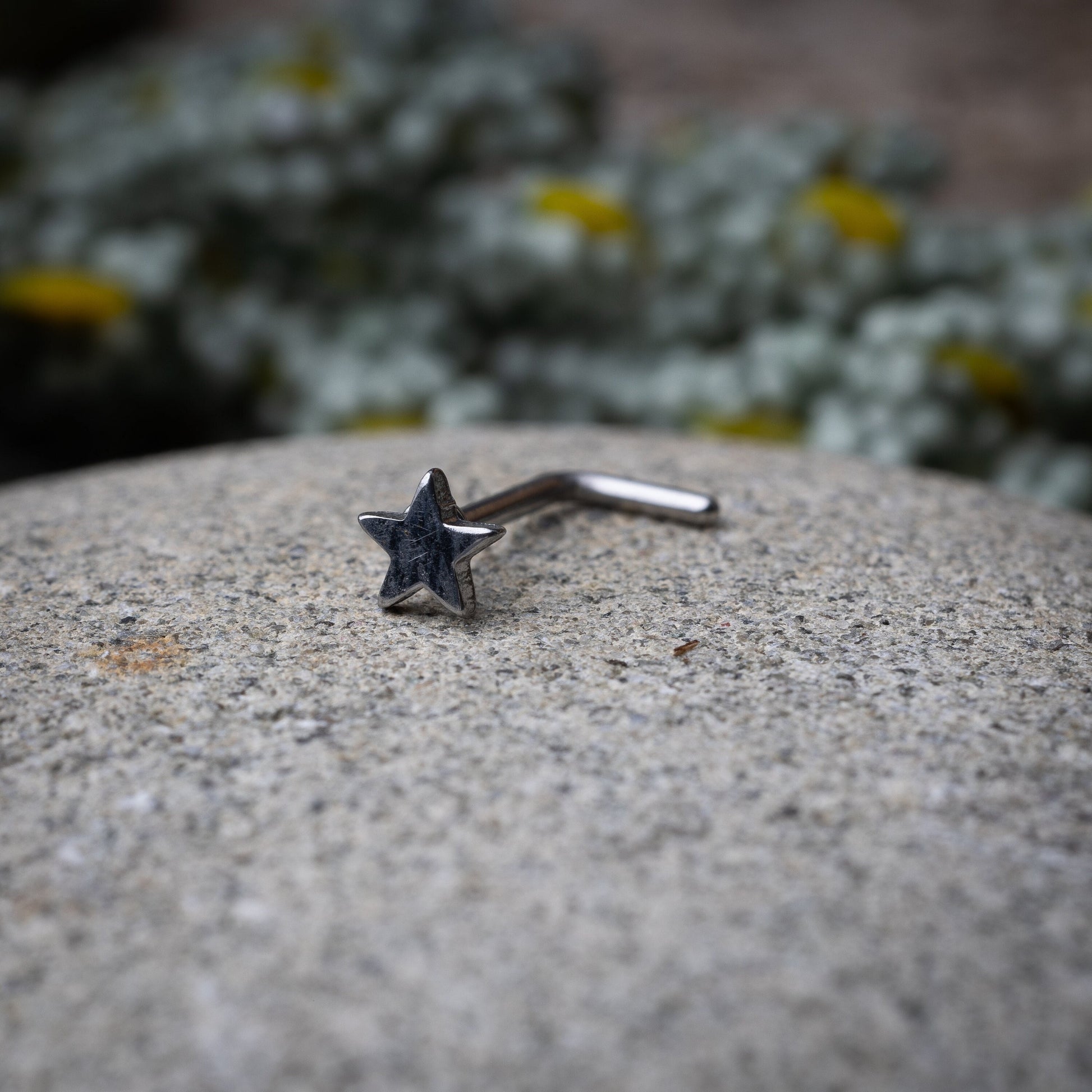 Sterling silver nose stud with a star-shaped design, displayed on a stone background.