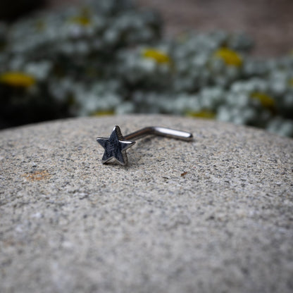 Sterling silver nose stud with a star-shaped design, displayed on a stone background.