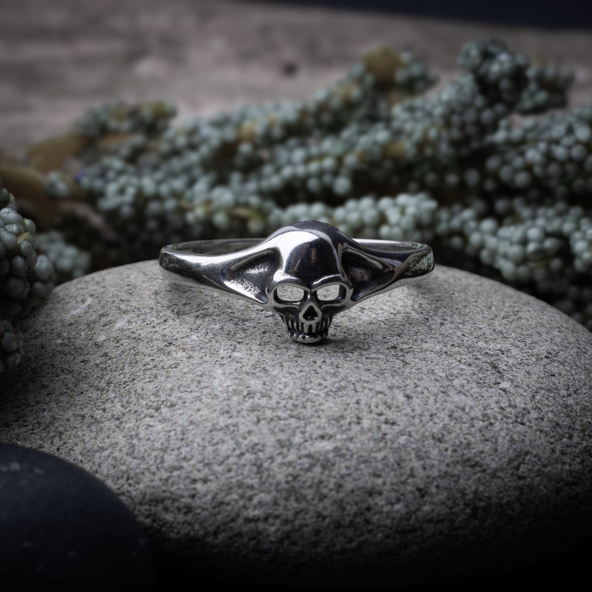 Sterling silver ring featuring a detailed skull design, displayed on a stone background.