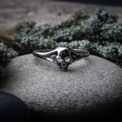 Sterling silver ring featuring a detailed skull design, displayed on a stone background.