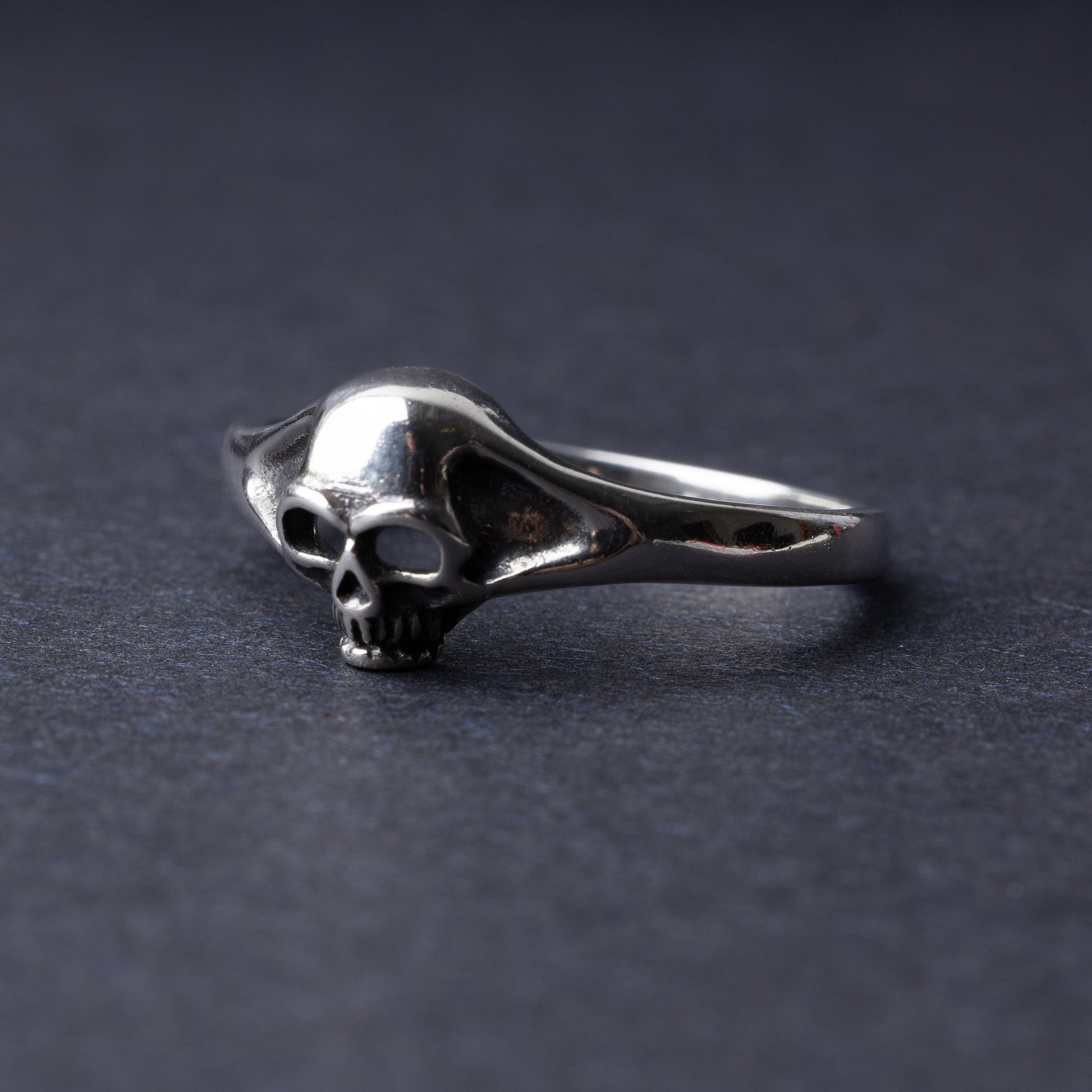 Sterling silver ring featuring a detailed skull design, displayed on a dark background.