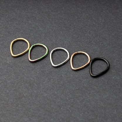A collection of teardrop-shaped clickers in gold, rainbow, silver, rose gold, and black finishes arranged on a dark background.