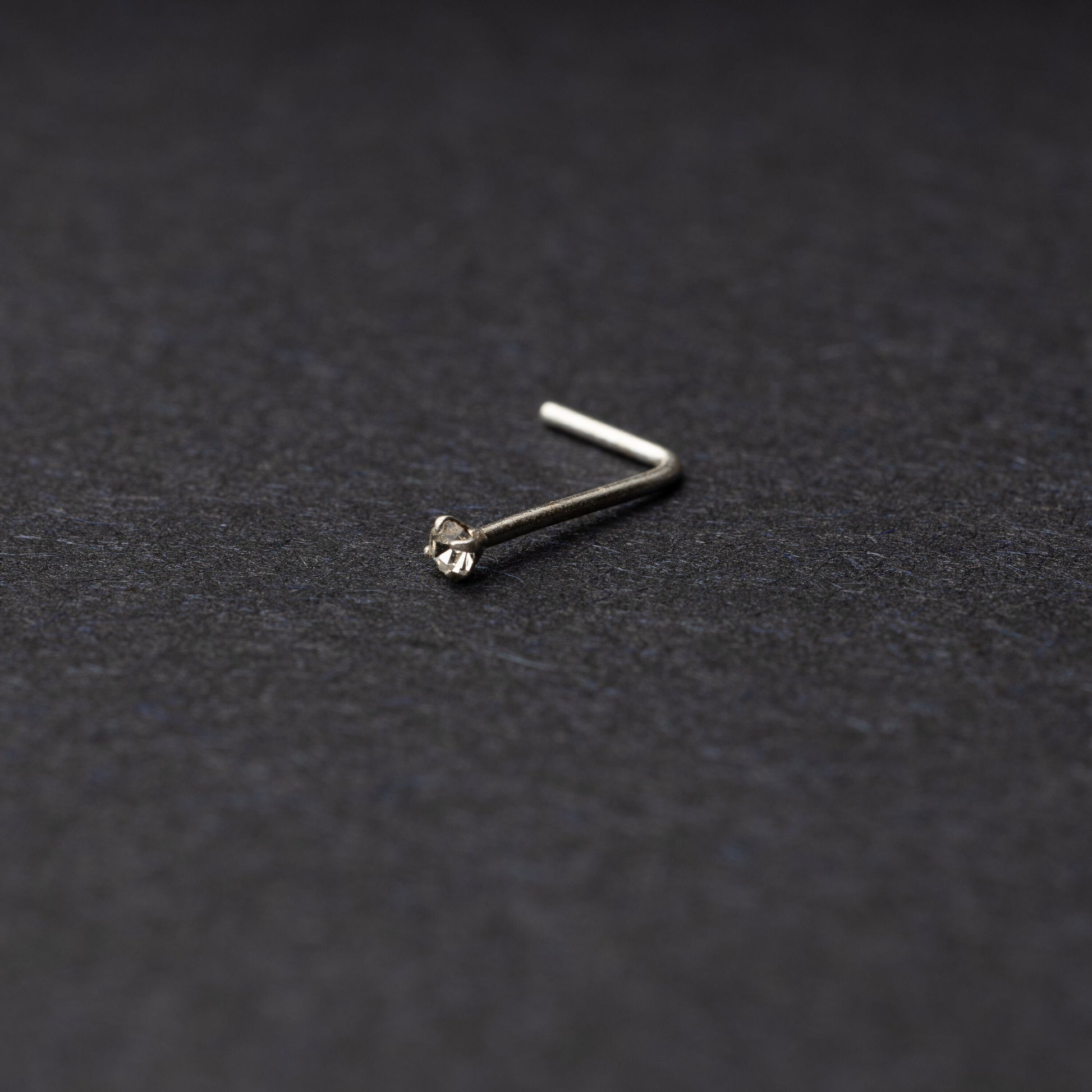 925 sterling silver nose stud with a small crystal accent, displayed on a dark textured background.