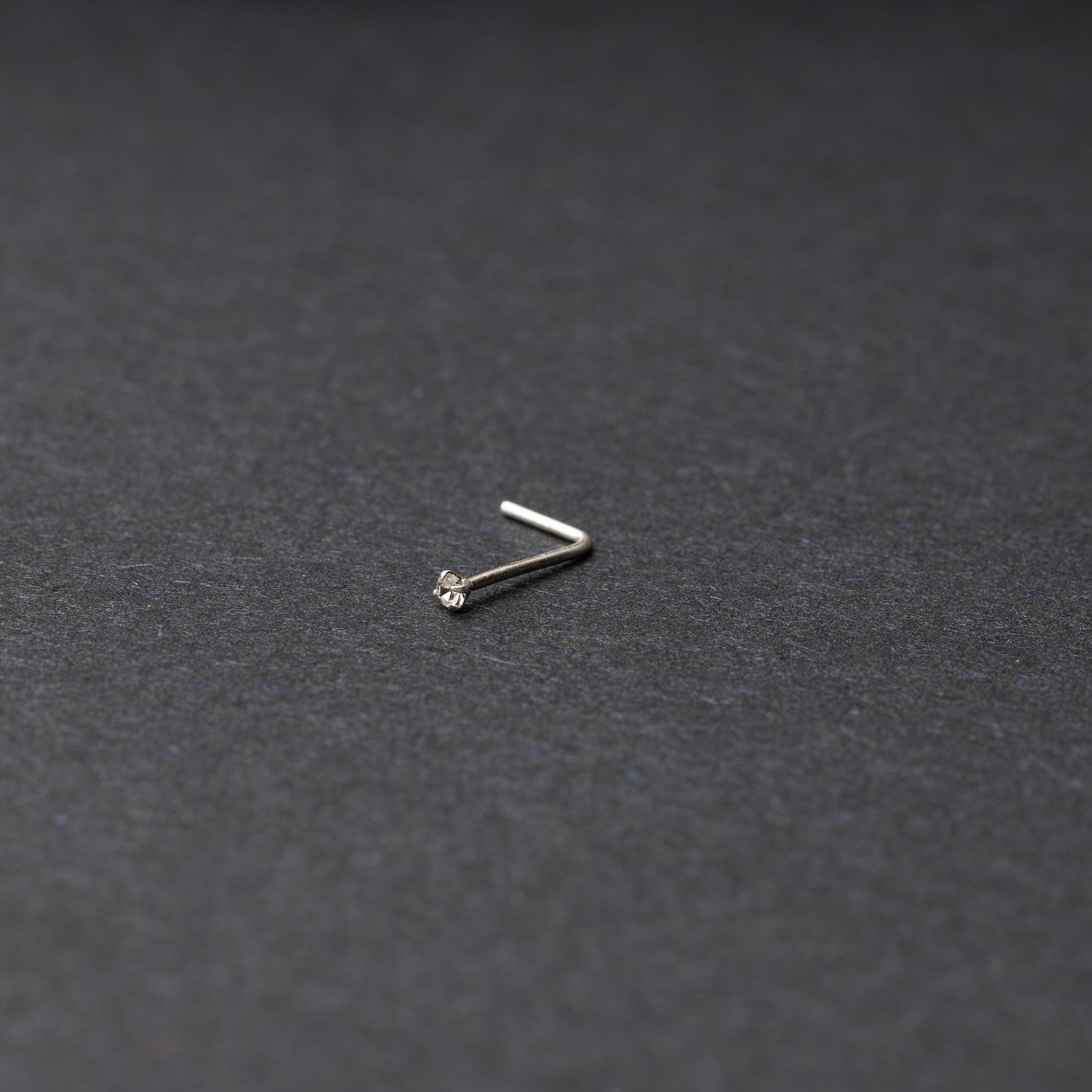 925 sterling silver nose stud with a small crystal accent, displayed on a dark textured background.