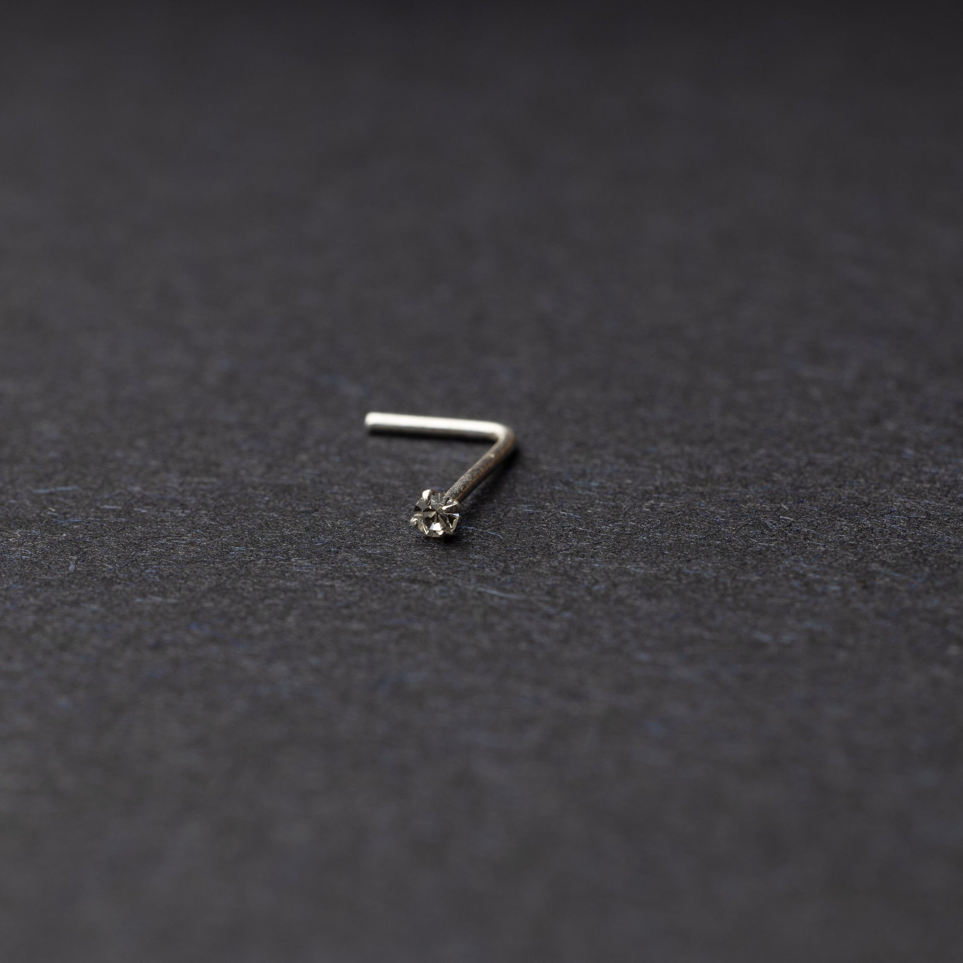 925 sterling silver nose stud with a small crystal accent, displayed on a dark textured background.