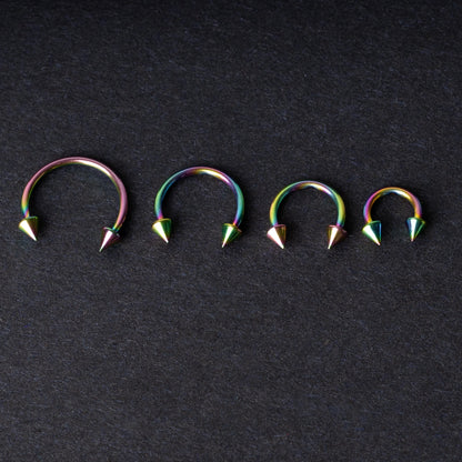 Titanium horseshoe hoops with spike ends, featuring a colorful rainbow finish, displayed on a dark textured background.