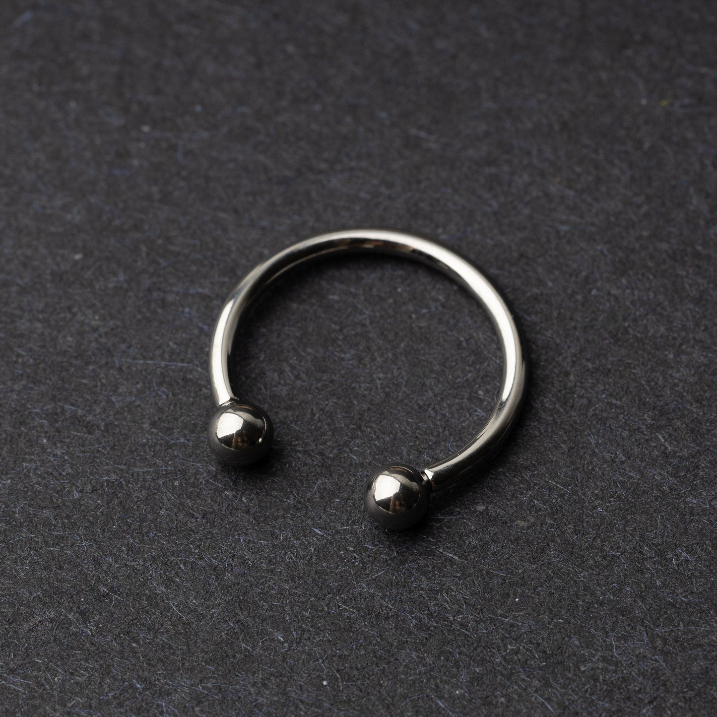 Titanium horseshoe ring with ball ends, displayed on a dark textured background.