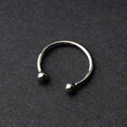 Titanium horseshoe ring with ball ends, displayed on a dark textured background.