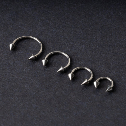 Four titanium horseshoe hoops with pointed cone ends, lined up on a dark background.