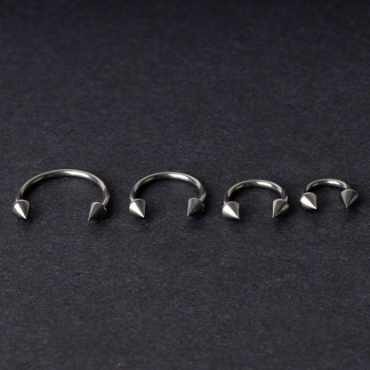 Four titanium horseshoe hoops with pointed cone ends, lined up on a dark background.