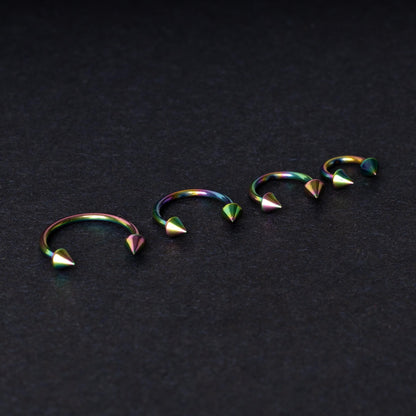 Titanium horseshoe hoops with spike ends, featuring a colorful rainbow finish, displayed on a dark textured background.