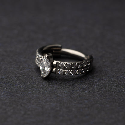A close-up of a marquise gemstone septum or helix clicker with dual rows of sparkling gems displayed on a dark background.

