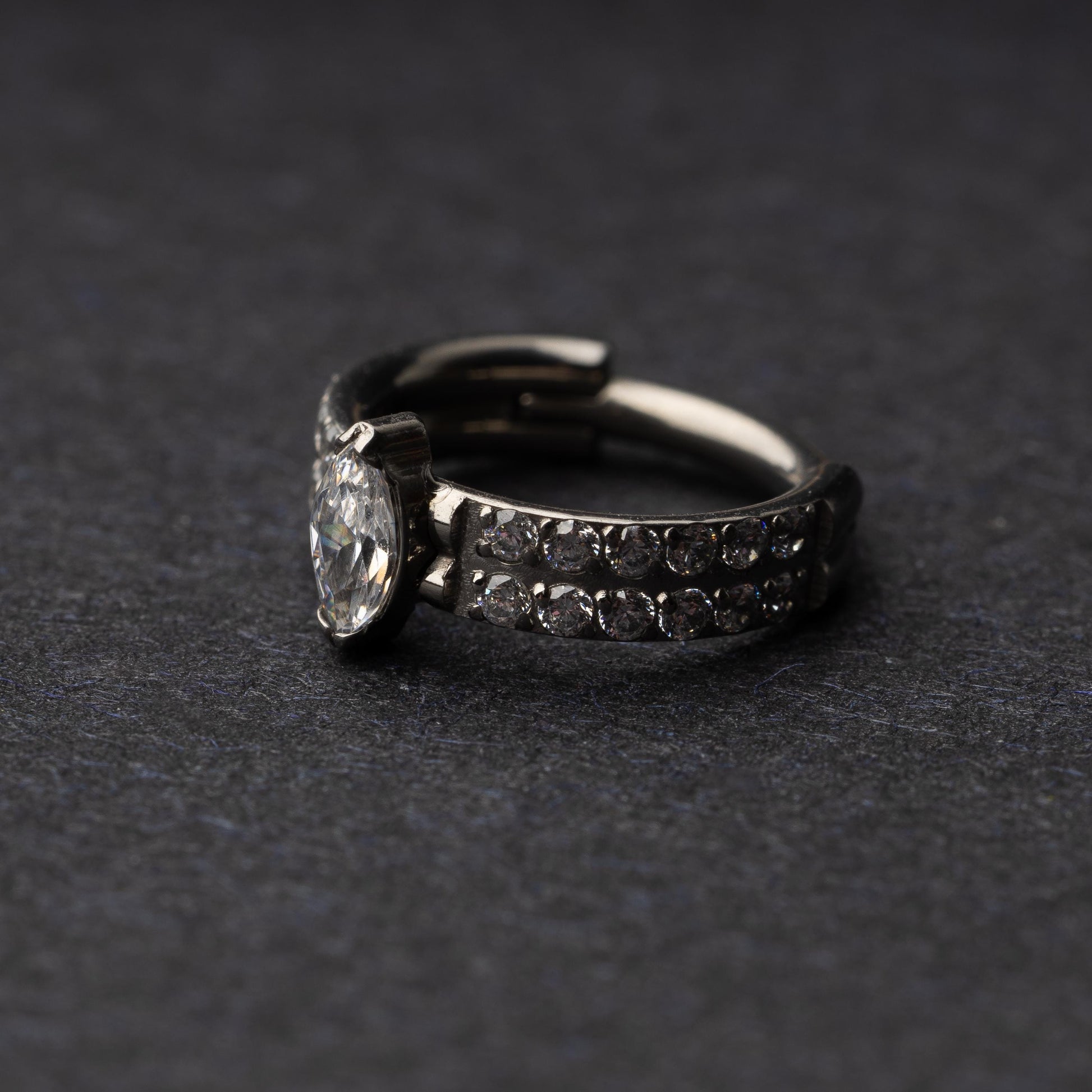 A close-up of a marquise gemstone septum or helix clicker with dual rows of sparkling gems displayed on a dark background.

