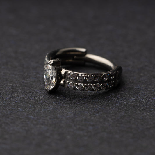 A close-up of a marquise gemstone septum or helix clicker with dual rows of sparkling gems displayed on a dark background.

