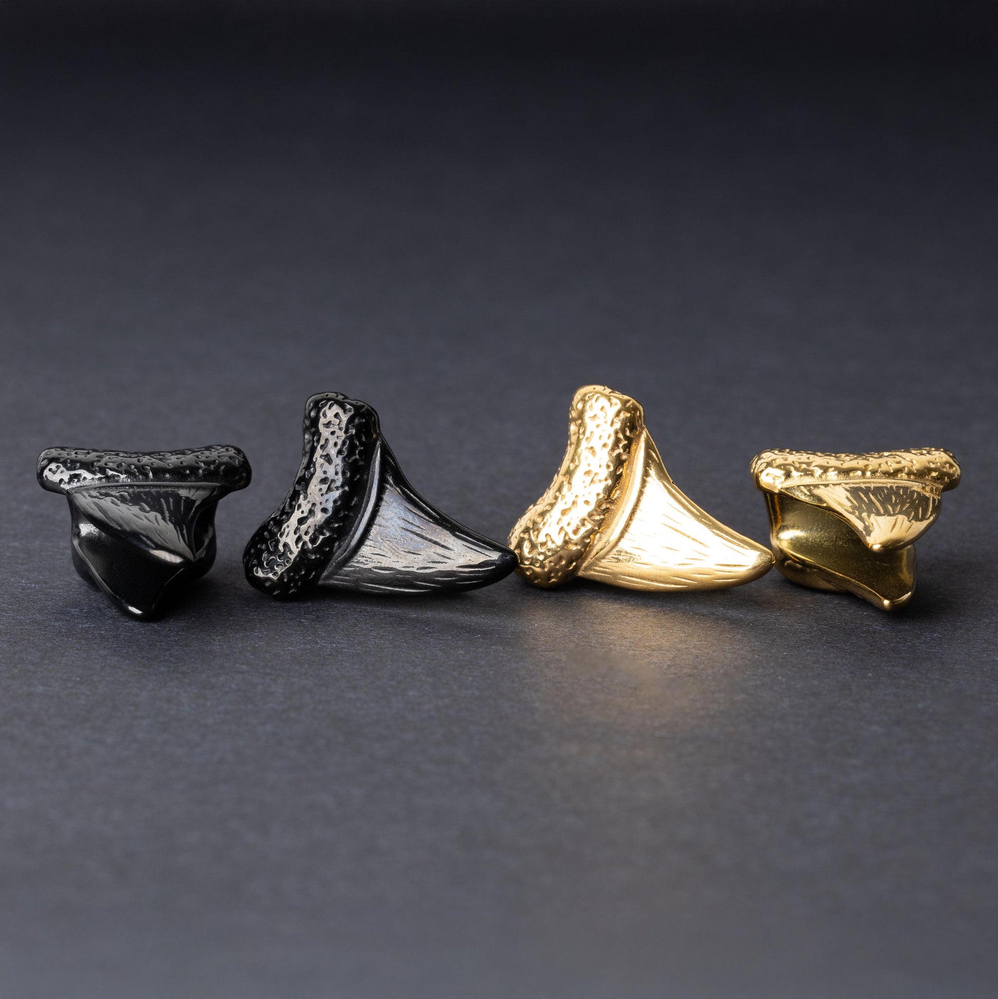 Close-up of gold and black tooth ear weights featuring textured detailing, displayed on a dark background.

