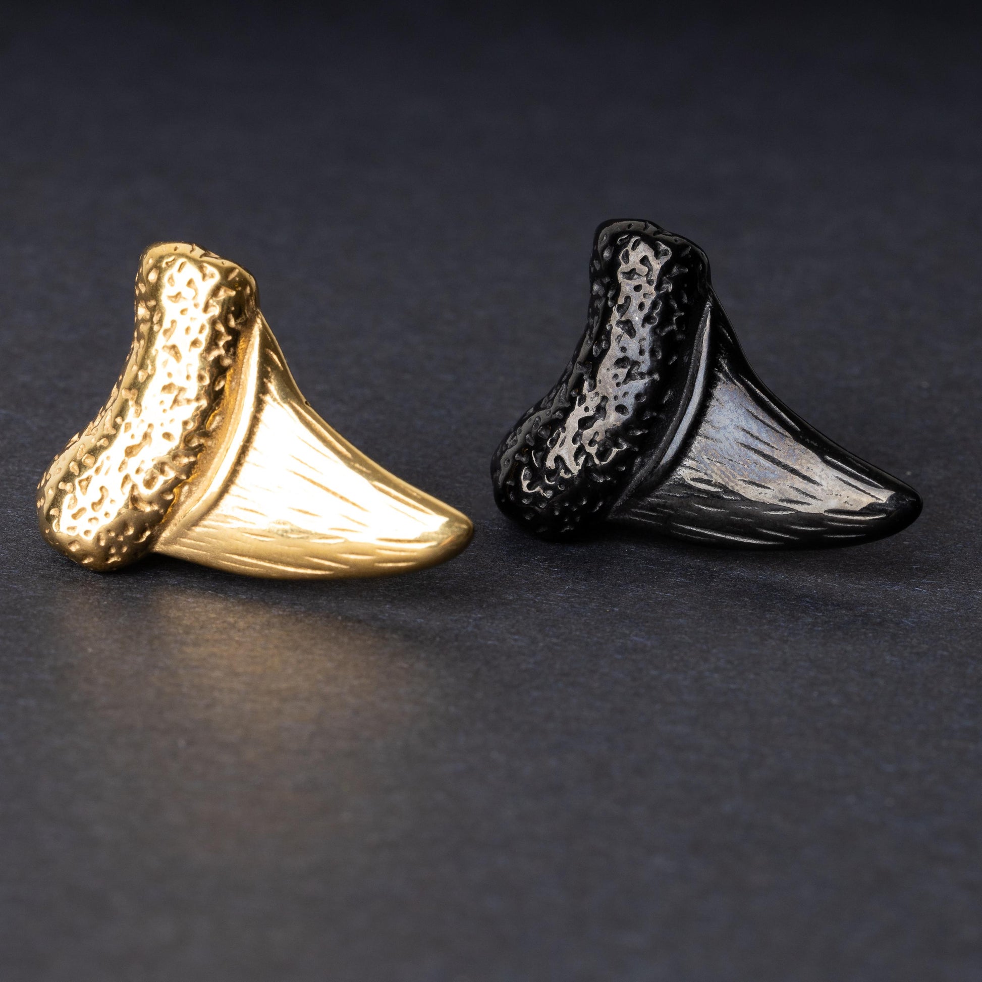 Close-up of gold and black tooth ear weights featuring textured detailing, displayed on a dark background.

