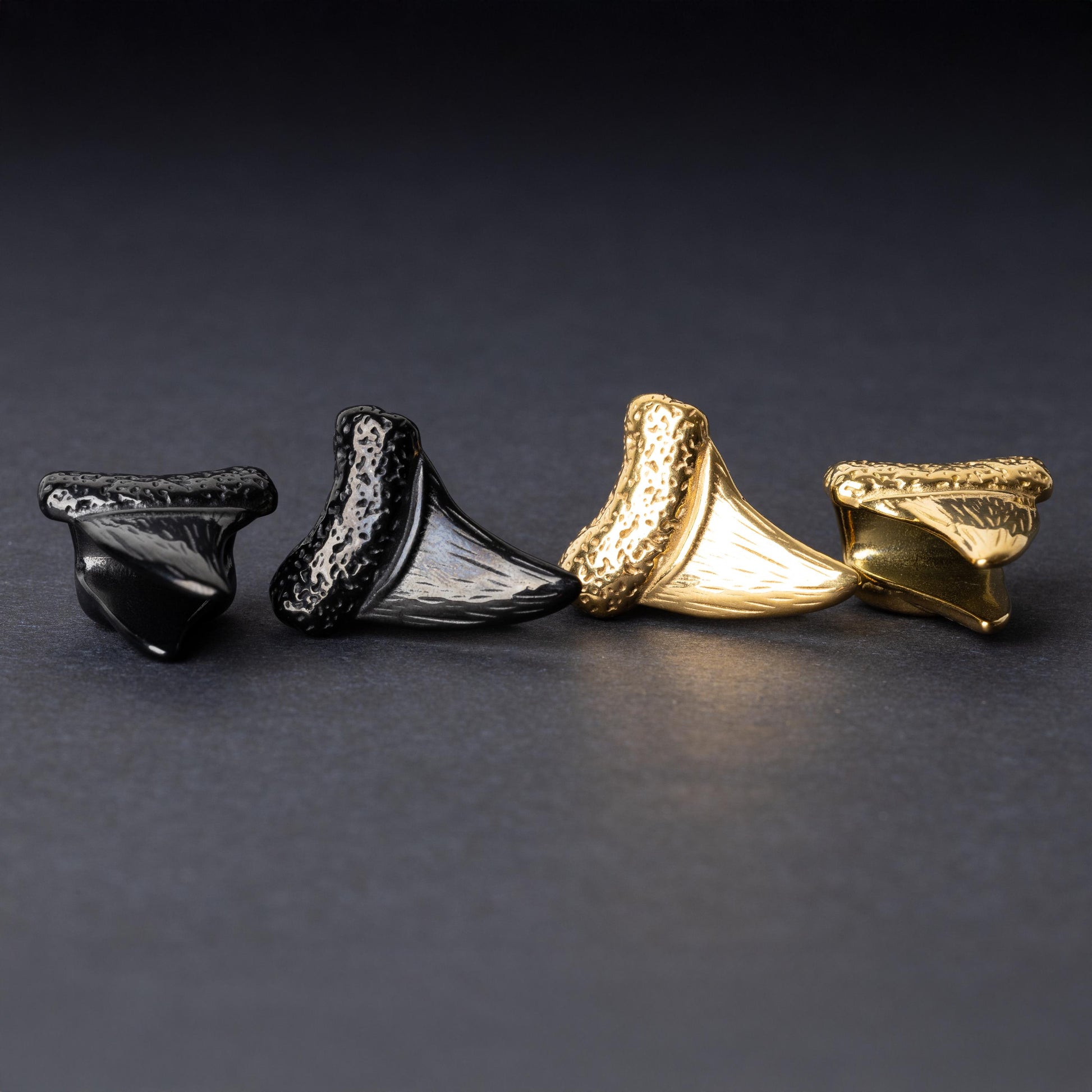 Close-up of gold and black tooth ear weights featuring textured detailing, displayed on a dark background.

