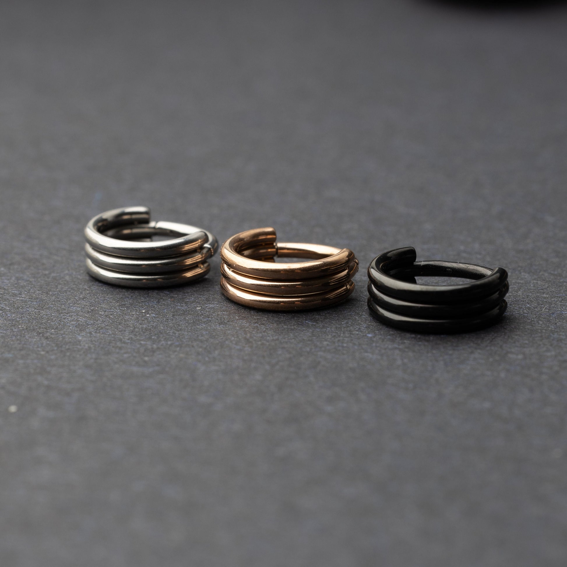 Triple-band seamless hoop rings in silver, gold, and black finishes displayed on a dark background, highlighting their sleek and modern design.