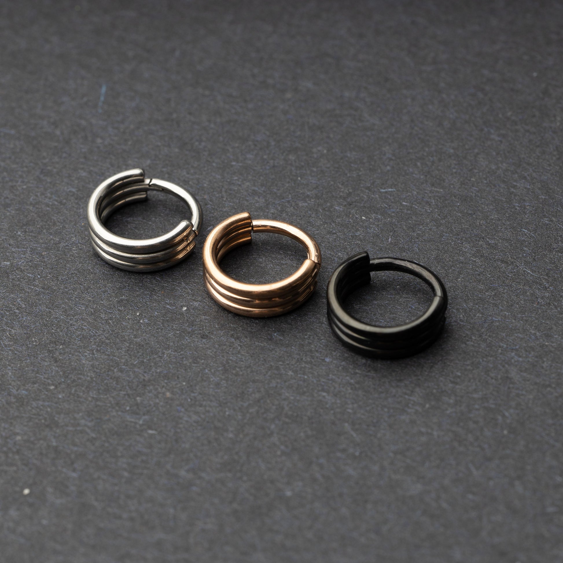 Triple-band seamless hoop rings in silver, gold, and black finishes displayed on a dark background, highlighting their sleek and modern design.