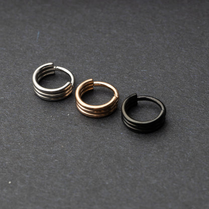 Triple-band seamless hoop rings in silver, gold, and black finishes displayed on a dark background, highlighting their sleek and modern design.