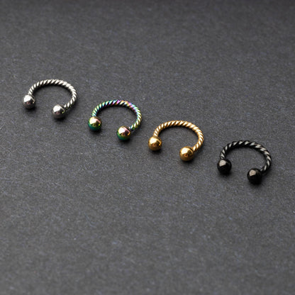 Twisted horseshoe barbells in silver, rainbow, gold, and black finishes displayed on a dark background, highlighting their bold and unique design.