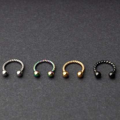 Twisted horseshoe barbells in silver, rainbow, gold, and black finishes displayed on a dark background, highlighting their bold and unique design.