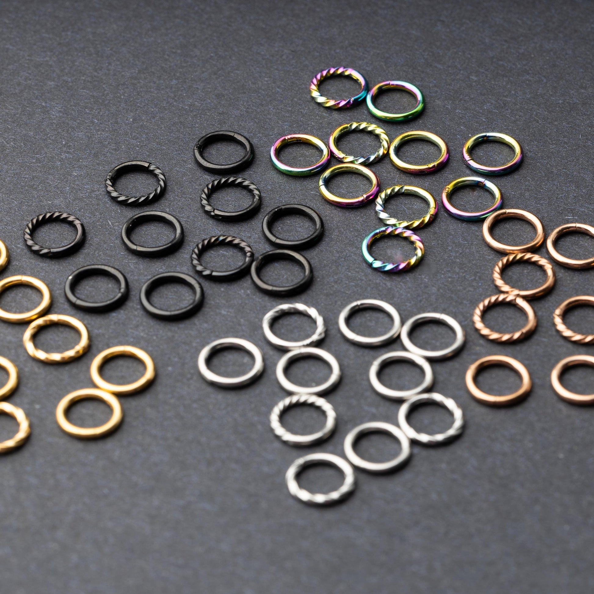 Set of clicker rings with smooth and twisted designs in various colors, displayed on a dark background.