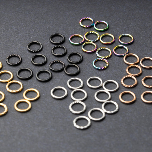Set of clicker rings with smooth and twisted designs in various colors, displayed on a dark background.