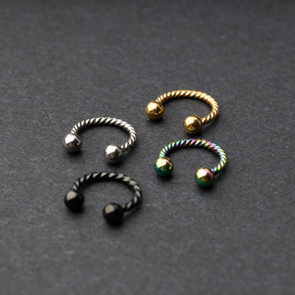 Twisted horseshoe barbells in silver, rainbow, gold, and black finishes displayed on a dark background, highlighting their bold and unique design.