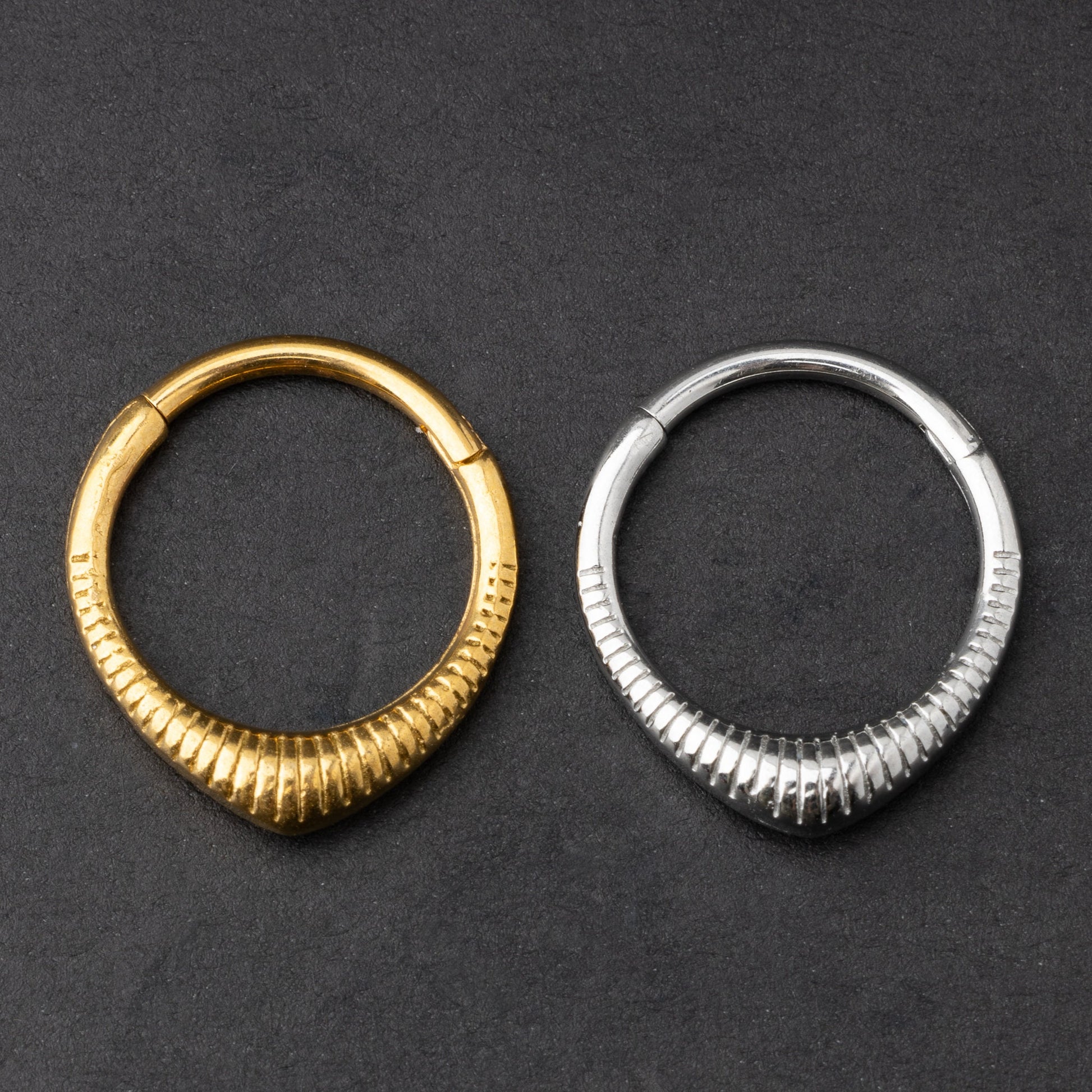 Gold and silver ribbed septum clicker jewelry displayed on a dark background, showcasing a sleek, modern design