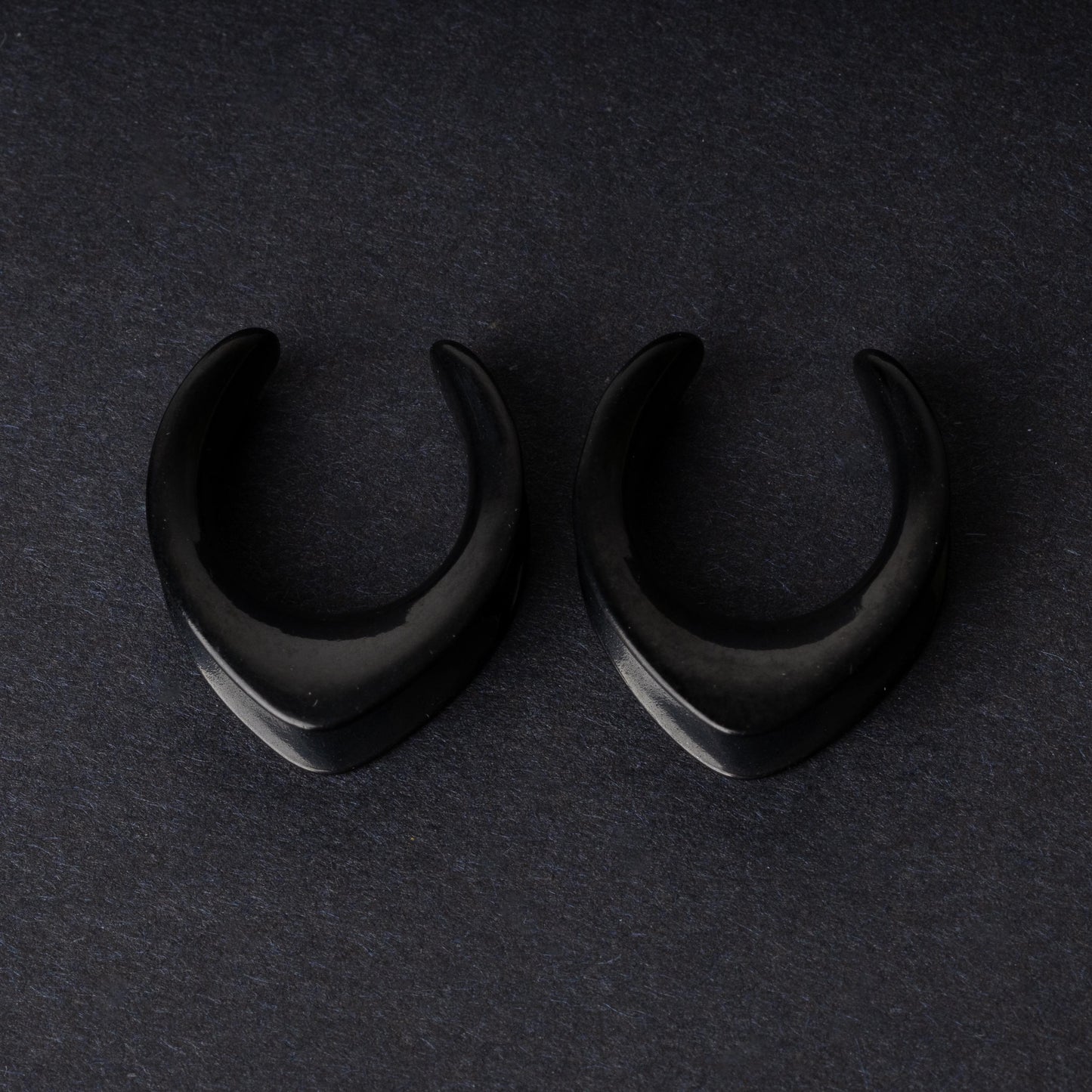 Double-flared metal tunnels for stretched ears in a gold finish, displayed on a dark background.
