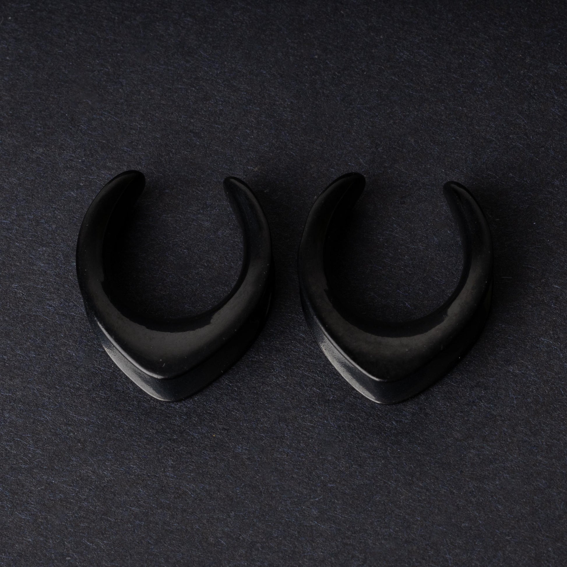 Double-flared metal tunnels for stretched ears in a gold finish, displayed on a dark background.
