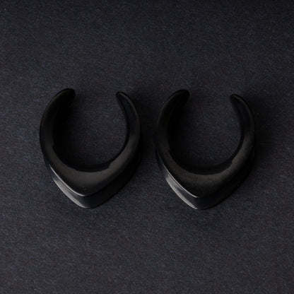 Double-flared metal tunnels for stretched ears in a gold finish, displayed on a dark background.

