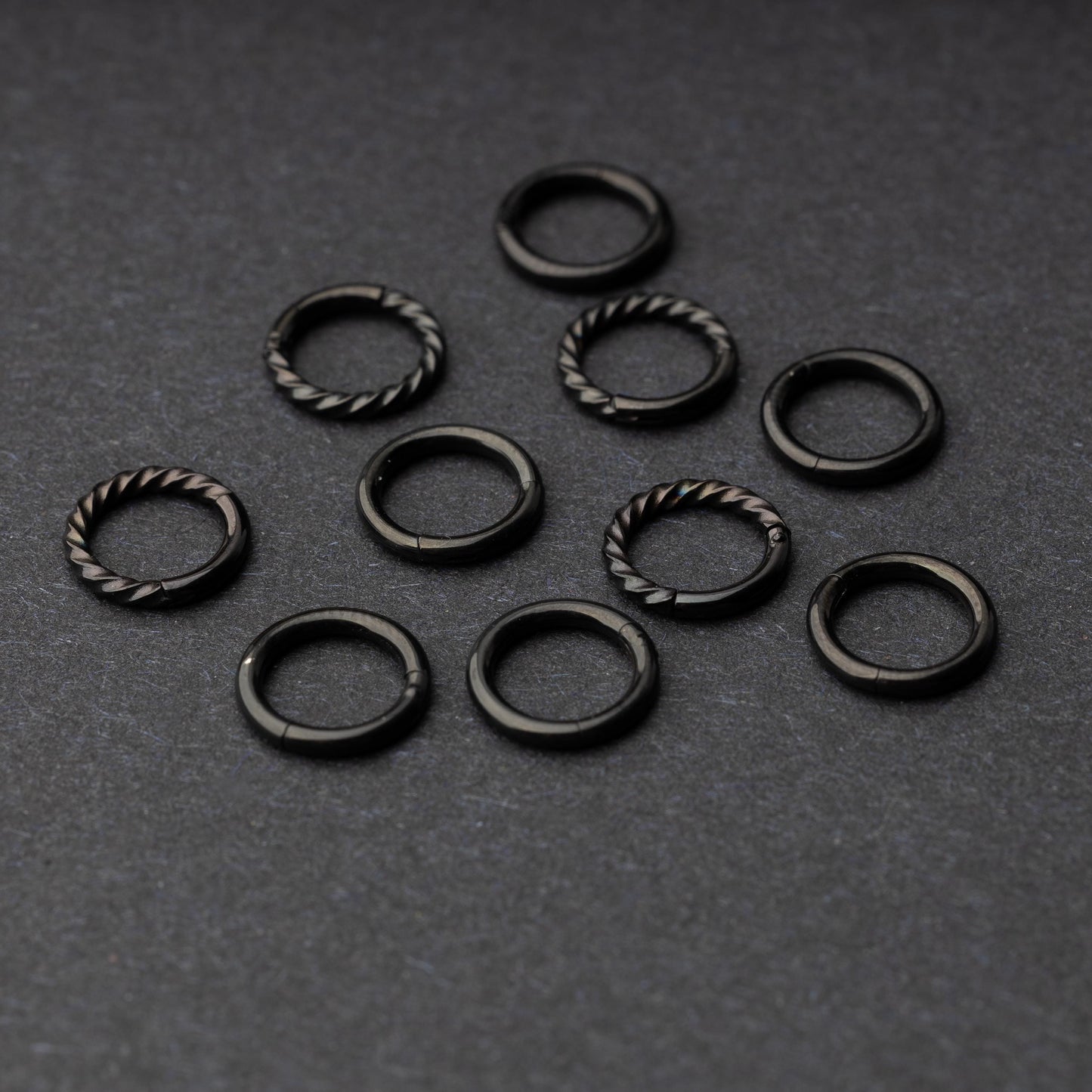 Set of black clicker rings with smooth and twisted designs, displayed on a dark background.