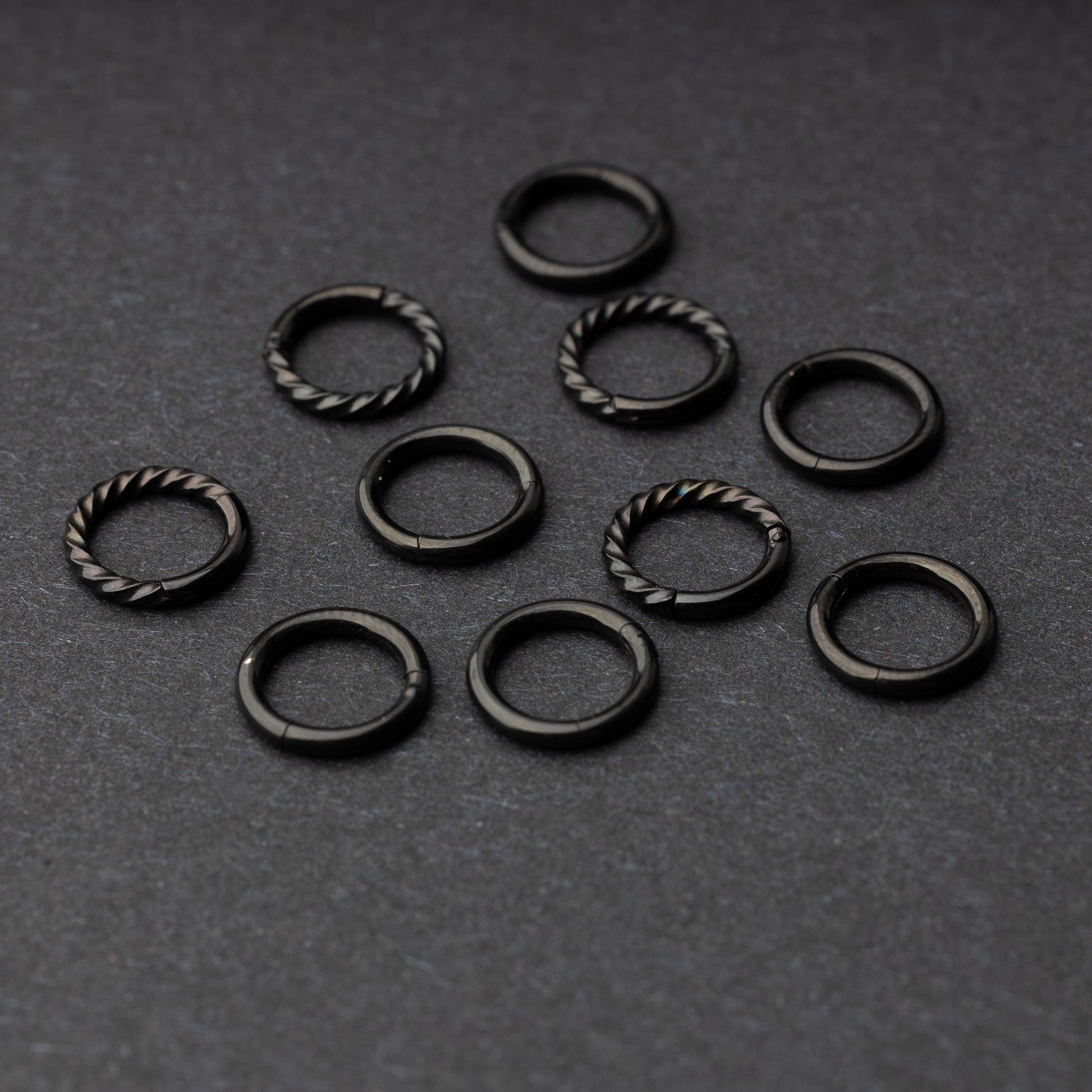 Set of black clicker rings with smooth and twisted designs, displayed on a dark background.
